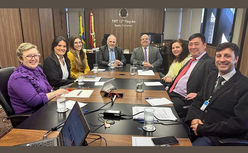 Quatro mulheres e quatro homens sentados em torno de uma mesa, sorridentes, posam para foto