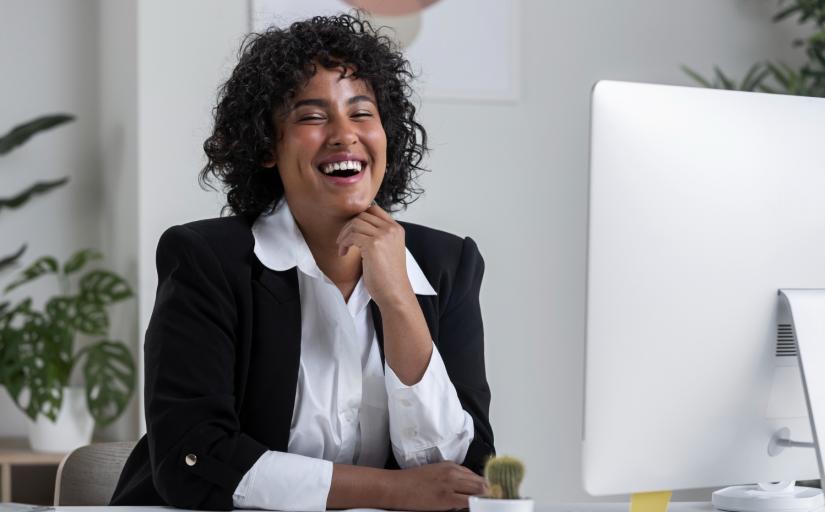 fotografia ilustrativa de uma mulher negra sorrindo de frente a um computador