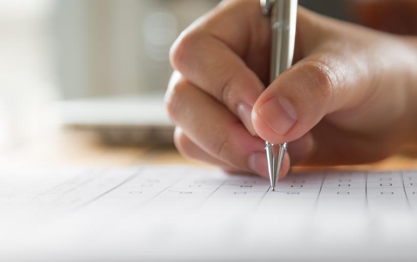 Mão branca escrevendo com uma caneta sobre um papael