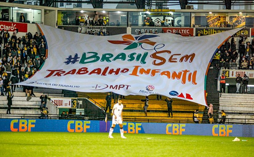 bandeira branca com os dizeres " Brasil sem Trabalho Infantil" em uma arquibancada de estádio