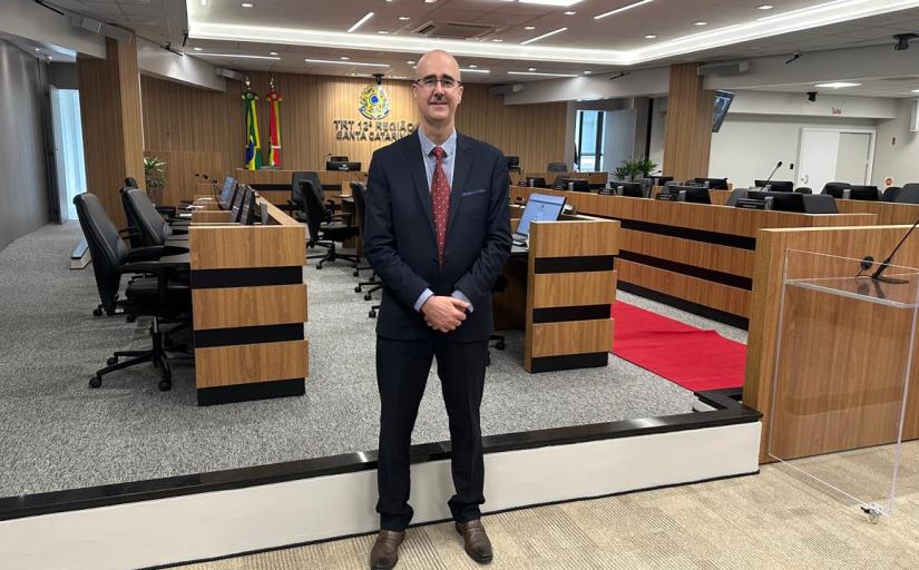 Reinaldo Branco de Moraes é um homem branco, que veste um terno, e está em pé na sala de sessões do Tribunal Pleno do TRT-12