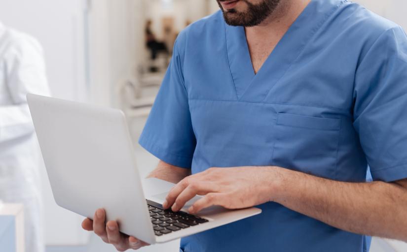 Tronco de um homem com jaleco azul mexendo em um notebook