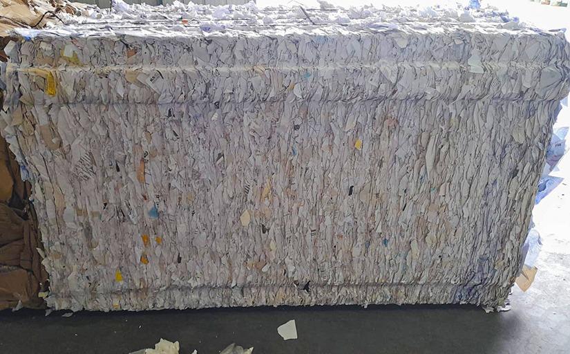 Fotografia de material doado para reciclagem. No chão, é possível ver um grande bloco aglutinado composto por papel de cor clara