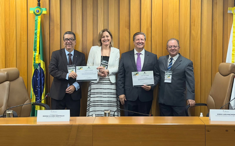 Quatro homens de terno e gravata e uma mulher posam para a foto segurando certificados