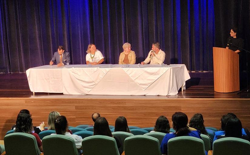 Quatro pessoas sentadas em frente a uma mesa que está sobre um palco. 