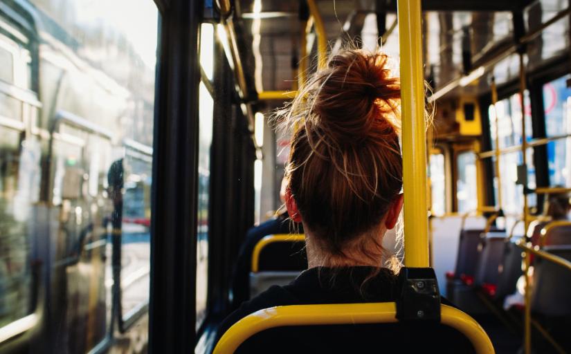 Foto mostra uma mulher, de costas, sentada em um banco de ônibus