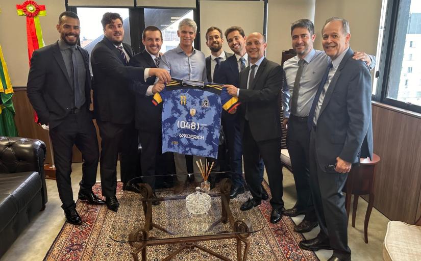 grupo de homens de terno posam para a foto. ao centro, um deles segura uma camisa de futebol