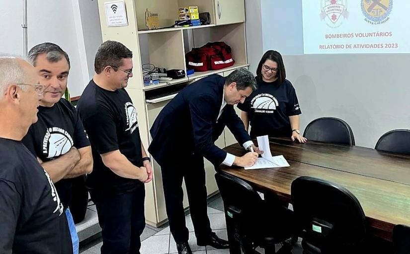 Varias pessoa de preto em pé, sendo uma debruçada sobre uma mesa assinando um papel