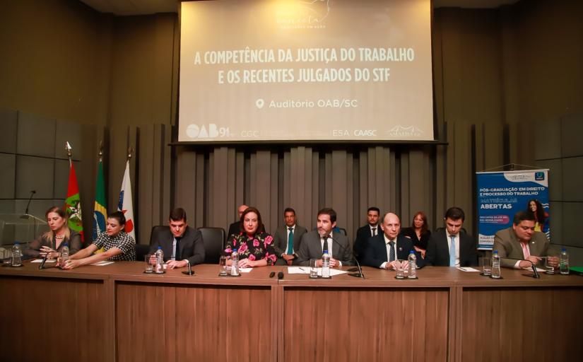 Foto mostra três mulheres e quatro homens sentados à mesa, no palco de um auditório