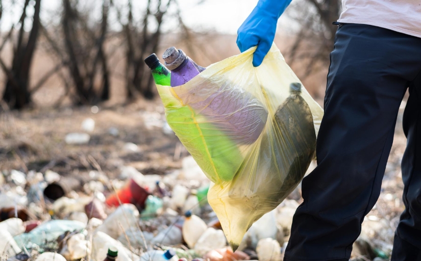 fotografia de um homem em um lixão carregando garrafas de plástico dentro de um saco de lixo