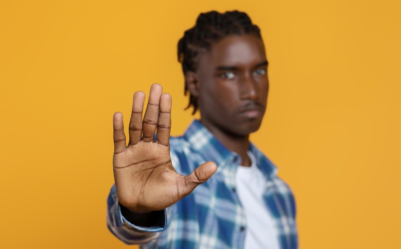 Fotografia ilustrativa de um jovem negro desfocado com a mão aberta para a câmera, expressando um gesto de "pare"