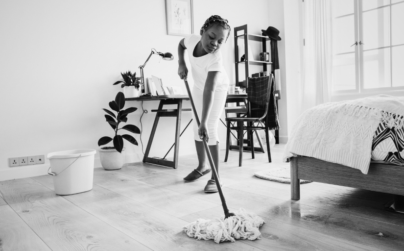 Foto em preto e branco mostra uma menina negra, de cerca de 13 anos, limpando o chão de um quarto com um esfregão