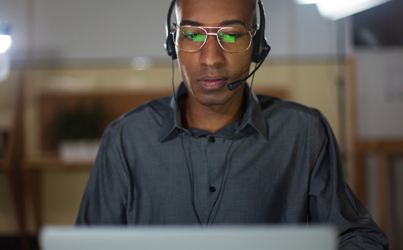 Imagem ilustrativa de homem negro de frente a um computador com headset