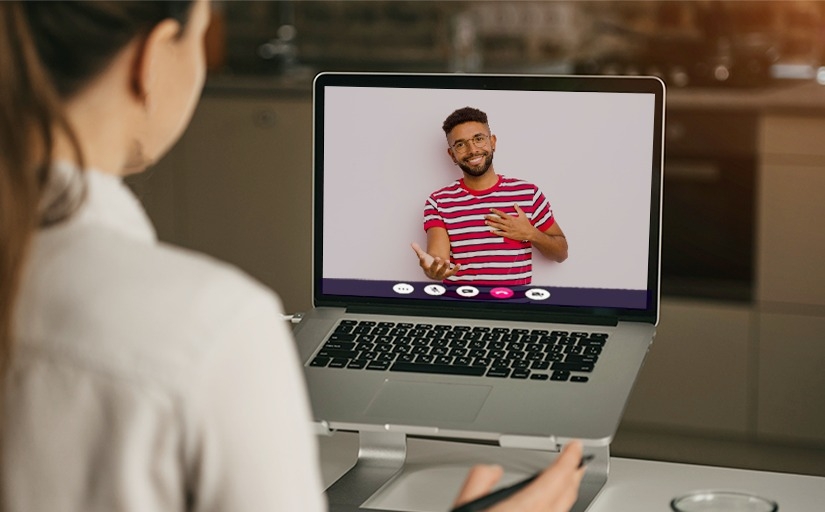 Foto de uma mulher branca de camisa branca com um notebook em chamada com um homem negro gesticulando