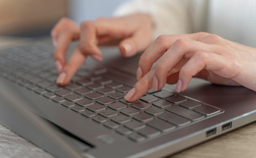 Fotografia ilustrativa de mãos femininas digitando no teclado de um notebook