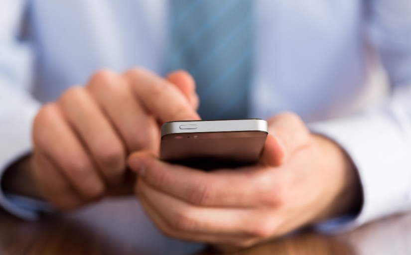 Fotografia ilustrativa de mãos de homem vestido formalmente mexendo no celular
