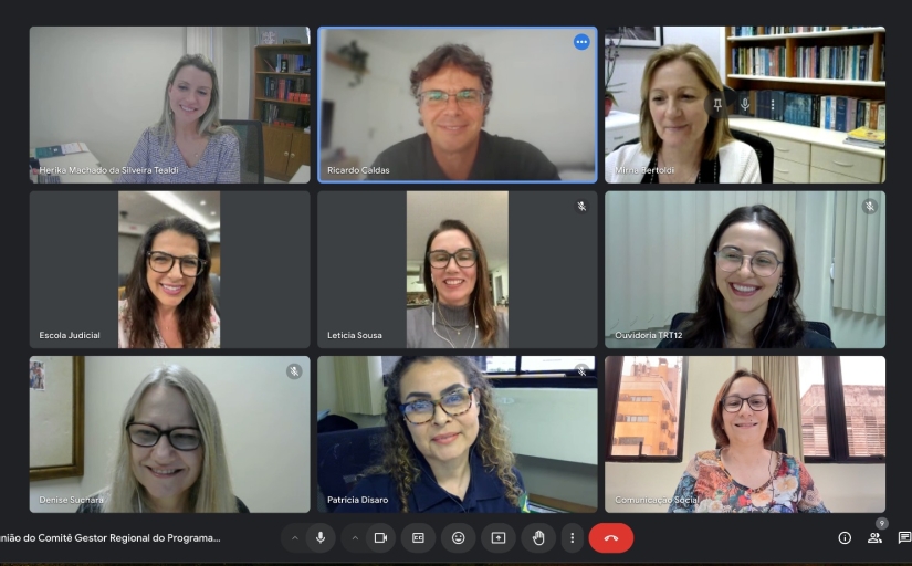 Esta é uma imagem de uma reunião virtual realizada por videoconferência, onde nove pessoas aparecem em suas respectivas janelas de vídeo, organizadas em uma grade. Todas as pessoas estão sorrindo, e há uma variedade de fundos, como estantes de livros e janelas, que mostram diferentes ambientes de trabalho. Os participantes parecem estar concentrados na reunião e estão todos vestidos de maneira profissional.