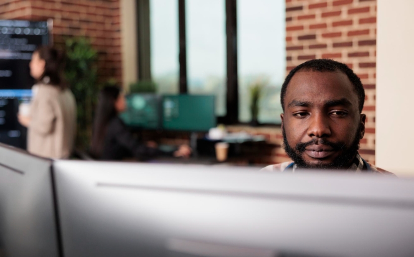 Fotografia ilustrativa de homem negro trabalhando diante de telas de um computador