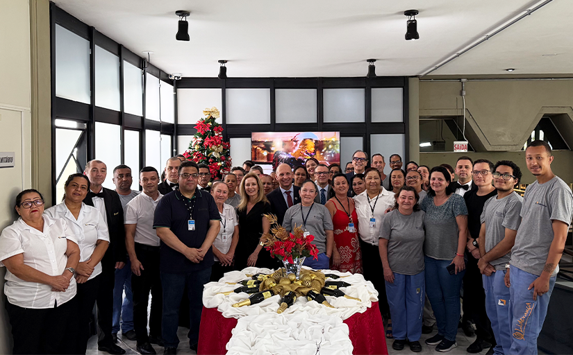 Dezenas de pessoas reunidas em torno de uma mesa com decoração natalina, a maioria delas vestindo uniforme branco ou cinza