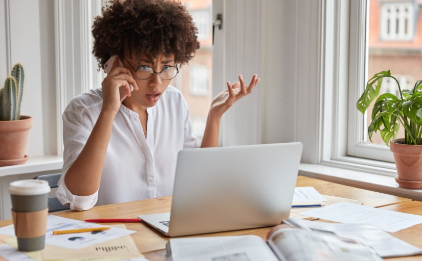 Mulher com expressão de choque olhando para o celular enquanto fala ao telefone