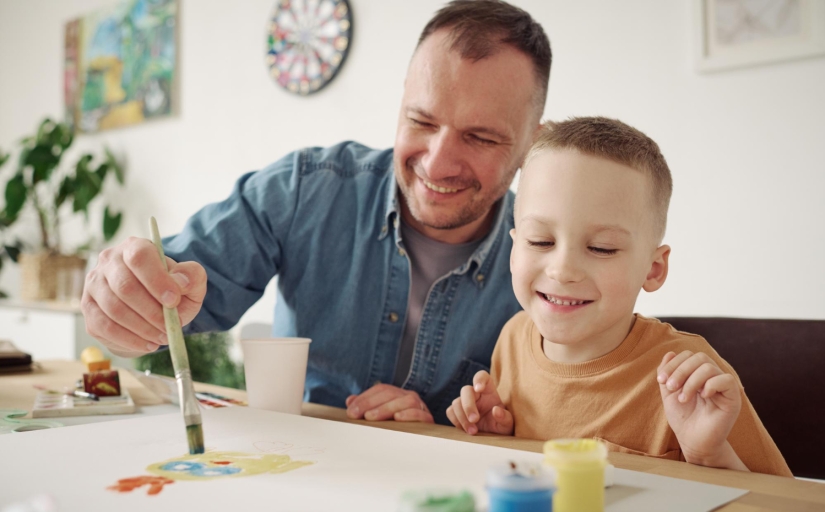 Pai e filho pintando uma folha com pincéis e tintas