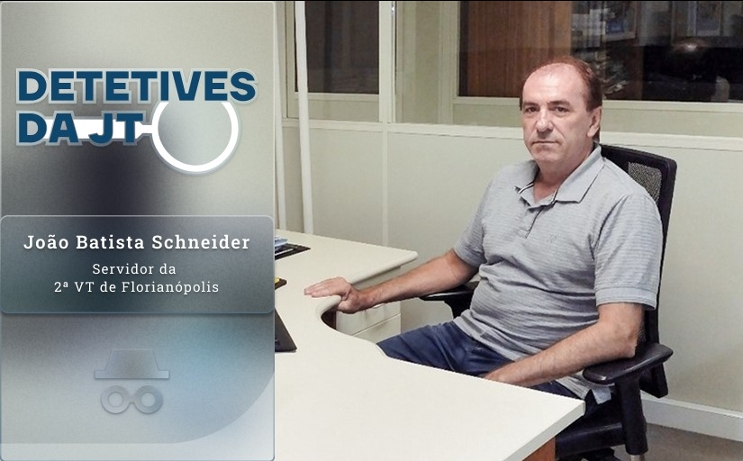 Detetives da JT: João Batista Schneider, servidor da 2ª VT de Florianópolis. Um homem branco sentando à mesa de trabalho, vestindo camisa polo cinza e olhando para a câmera