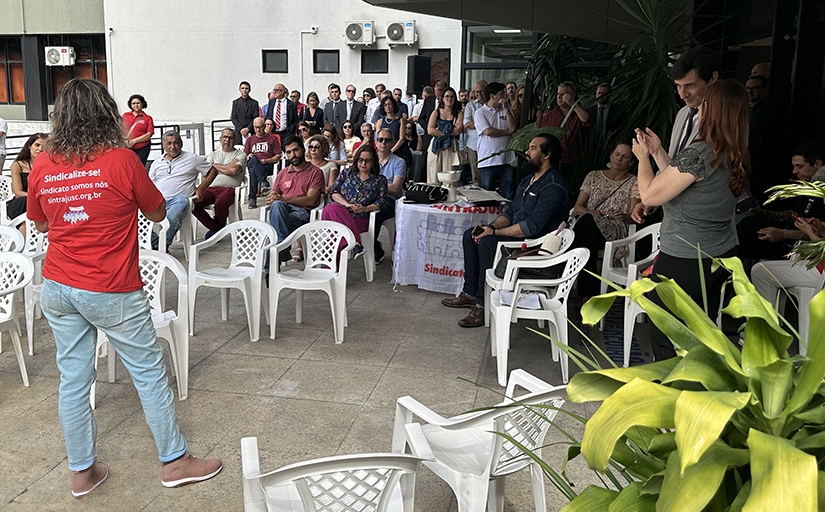 Pessoa de camiseta vermelha falando para um público sentado em cadeiras