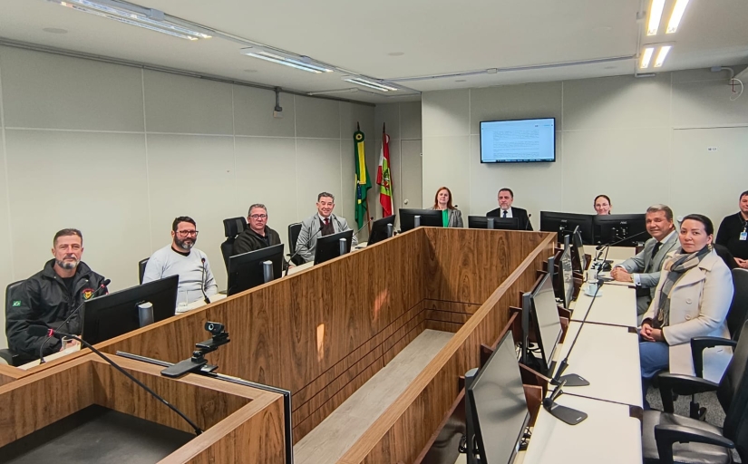 Grupo de homens e duas mulheres posam para foto, sentados ao redor de uma mesa em uma sala de audiências