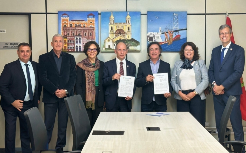 Duas mulheres e cinco homens estão em pé, sorrindo e posando para a foto, em uma sala de reuniões com quadros coloridos na parede