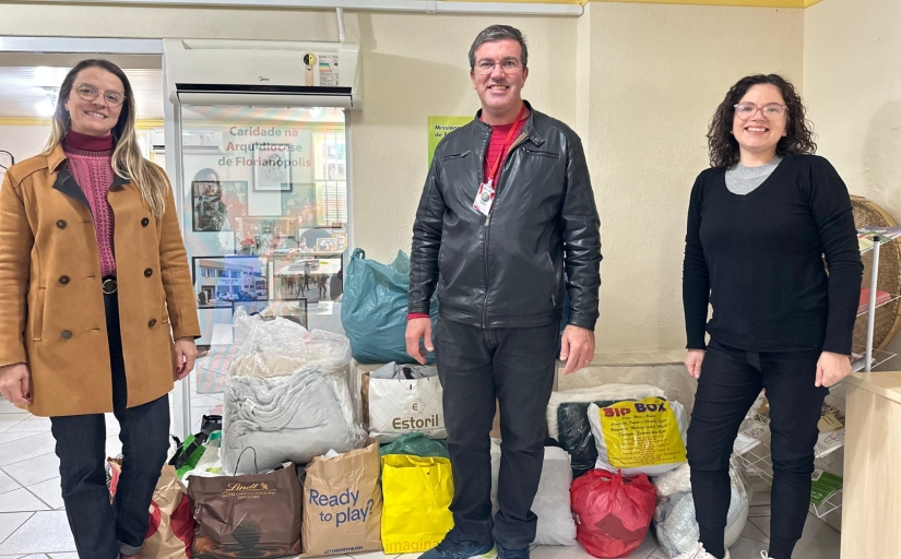 Três pessoas em pé posando par foto diante de bolsas com cobertores e roupas de inverno
