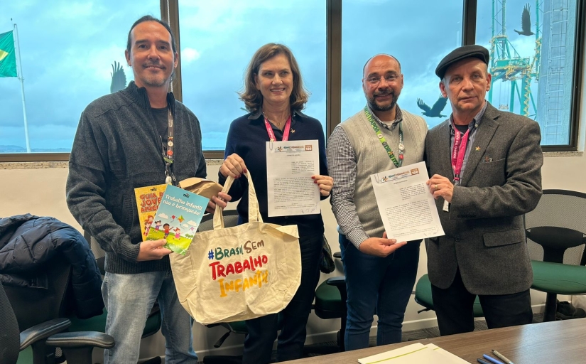 Quatro representantes posam com cartilhas e sacola da campanha Brasil Sem Trabalho Infantil após assinatura de parceria.