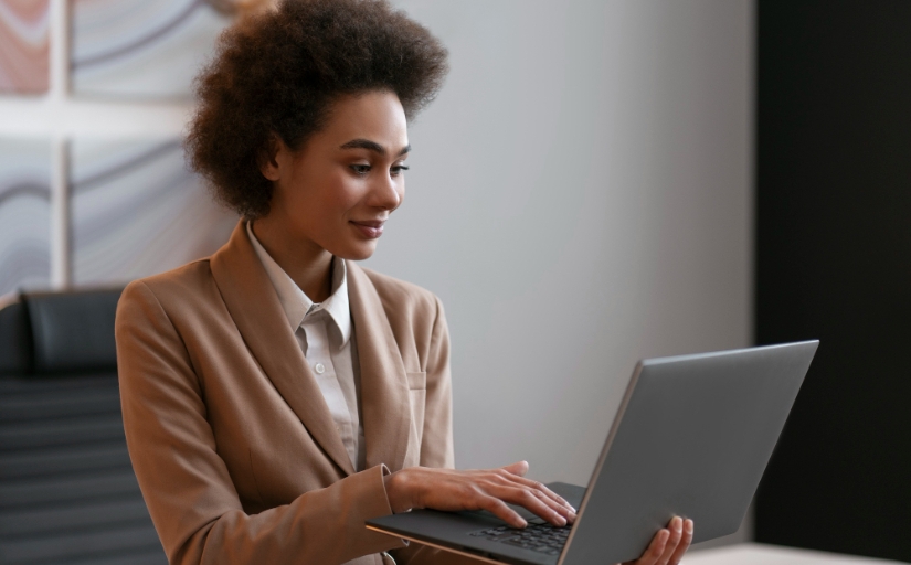 Fotografia ilustrativa de mulher negra vestida formalmente utilizando o notebook em um escritório