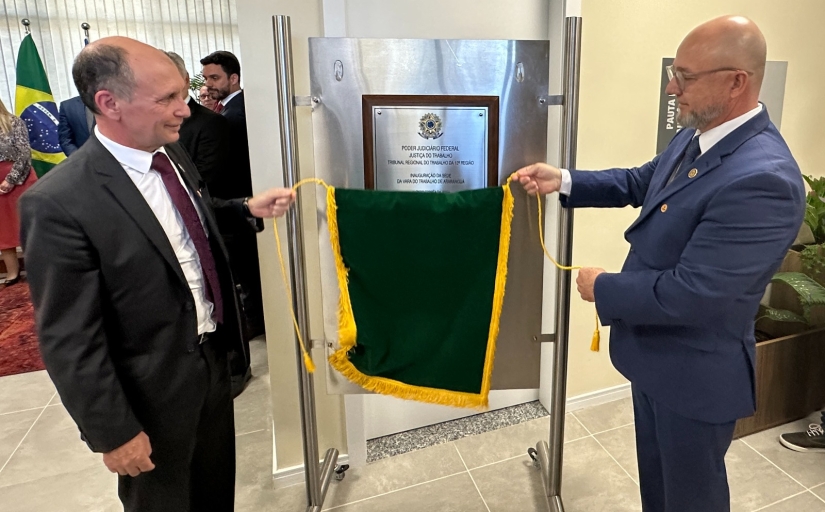 Dois homens de terno e gravata estão descerrando uma placa de inaguração
