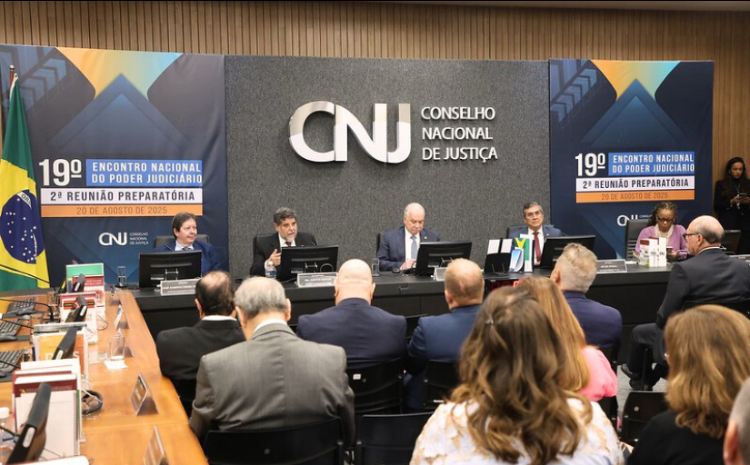 Quatro homens e uma mulher estão sentados em uma mesa de uma palestra. Pessoas estão assistindo. No fundo do palco tem um painel com o texto: CNJ