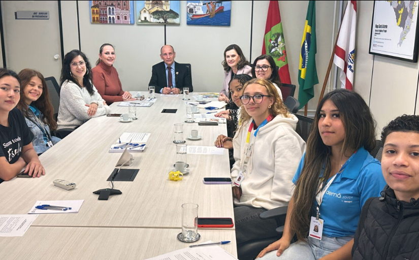 Seis jovens e cinco adultos estão sentados em uma mesa de reunião oval, posando para a foto