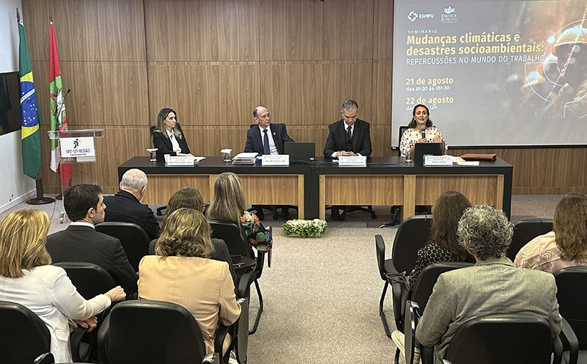 Mesa composta de quatro pessoas e público em primeiro plano assistindo palestra