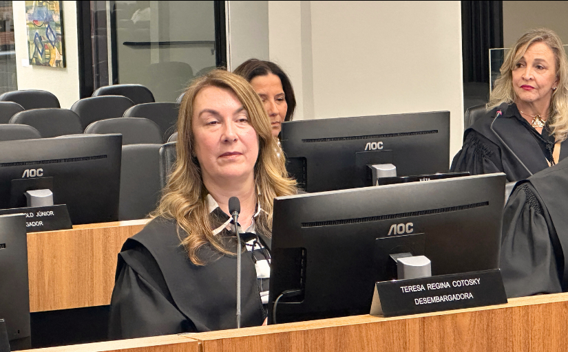Foto de uma mulher loira, sentada em um tribunal, vestida com toga