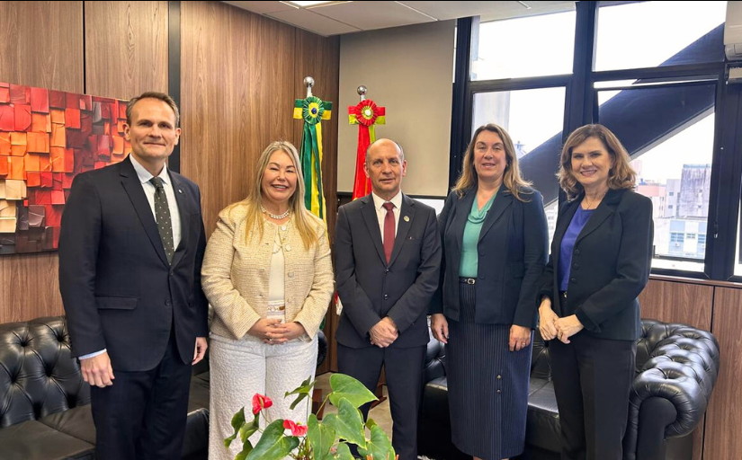 Dois homens de terno e gravata e três mulheres vestidas formalmente estão em pé, posando para a foto