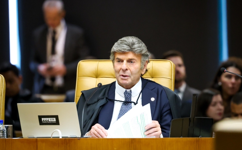 Foto do ministro do STF, Luiz Fux (homem de cabelo grisalho), sentado em uma mesa