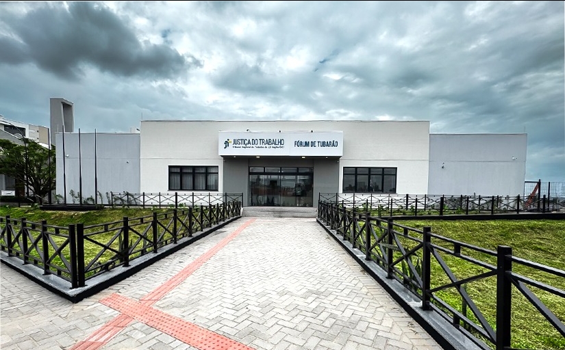 Prédio térreo em cor cimento queimado, ladeado por dois gramados. Céu nublado