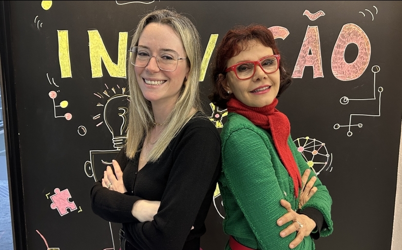 Duas mulheres, uma de costas para a outra, posam de braços cruzados