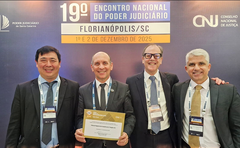 Quatro homens de terno escuro posam para foto. Um deles segura um certificado. 