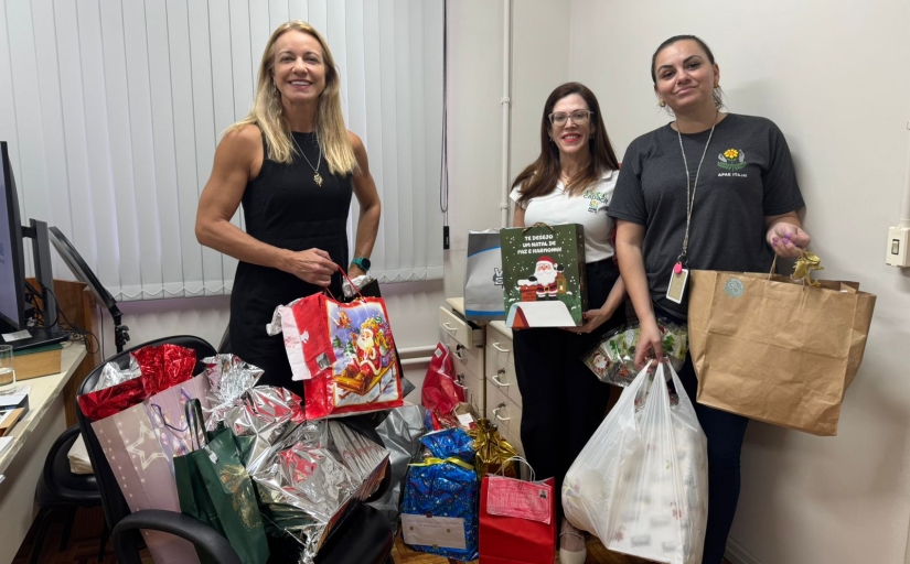 Foto de três mulheres exibindo presentes que foram entregues à entidade
