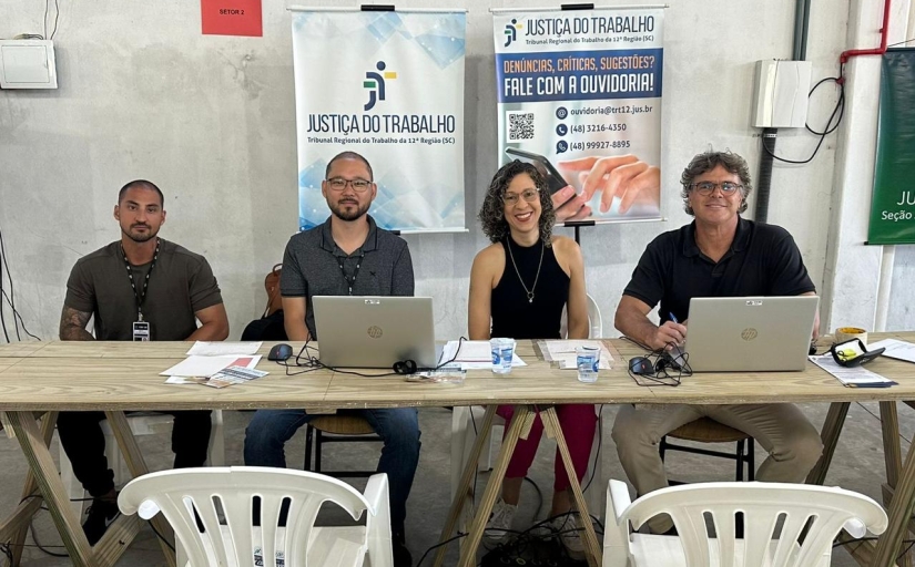 Imagem de uma mulher e três homens sentados em uma mesa com computador