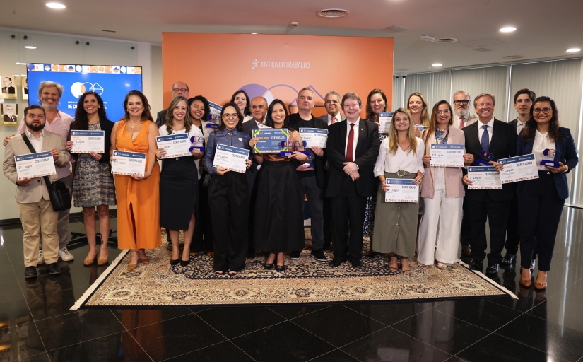 Grupo de cerca de 30 pessoas posam para foto, de pé, exibindo certificados e troféus.