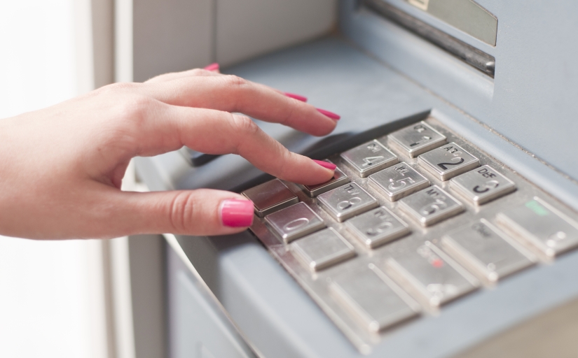 Foto que mostra a mão de uma mulher digitando no teclado de um caixa automático