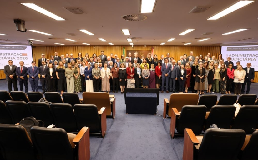 Cerca de 50 pessoas posam para a foto em pé, à frente de um auditório