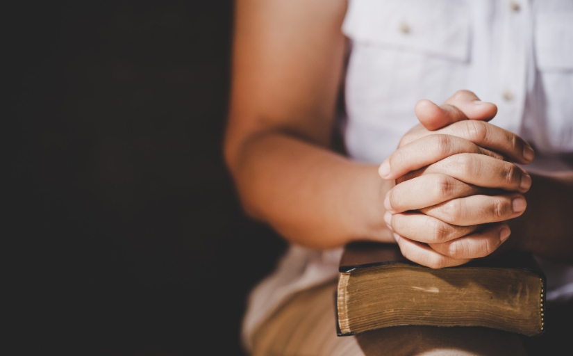 Fotografia ilustrativa de mulher com mãos entrelaçadas, apoiadas sobre um livro fechado