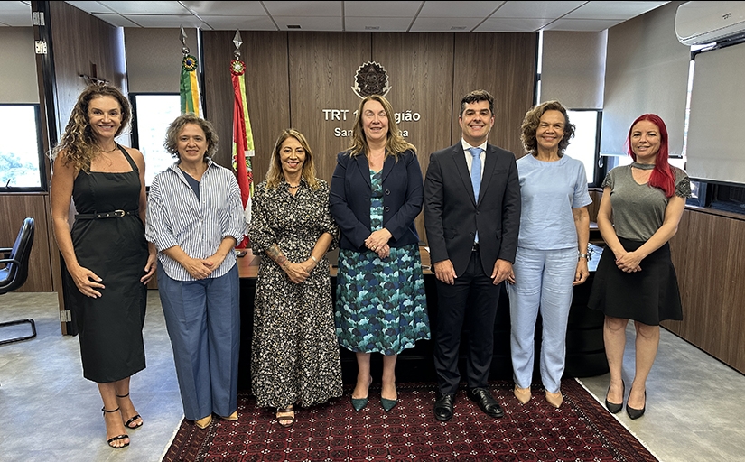 Seis mulheres vestidas formalmente e um homem de terno escuro posam de pé para a foto, sorridentes