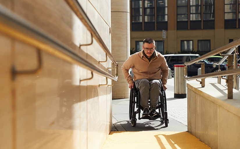 Homem em cadeira de rodas subindo rampa de acesso